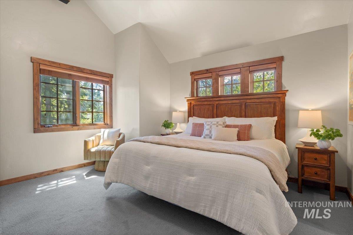 Vaulted ceiling bedroom featuring wood-framed windows, light gray walls, and carpet flooring