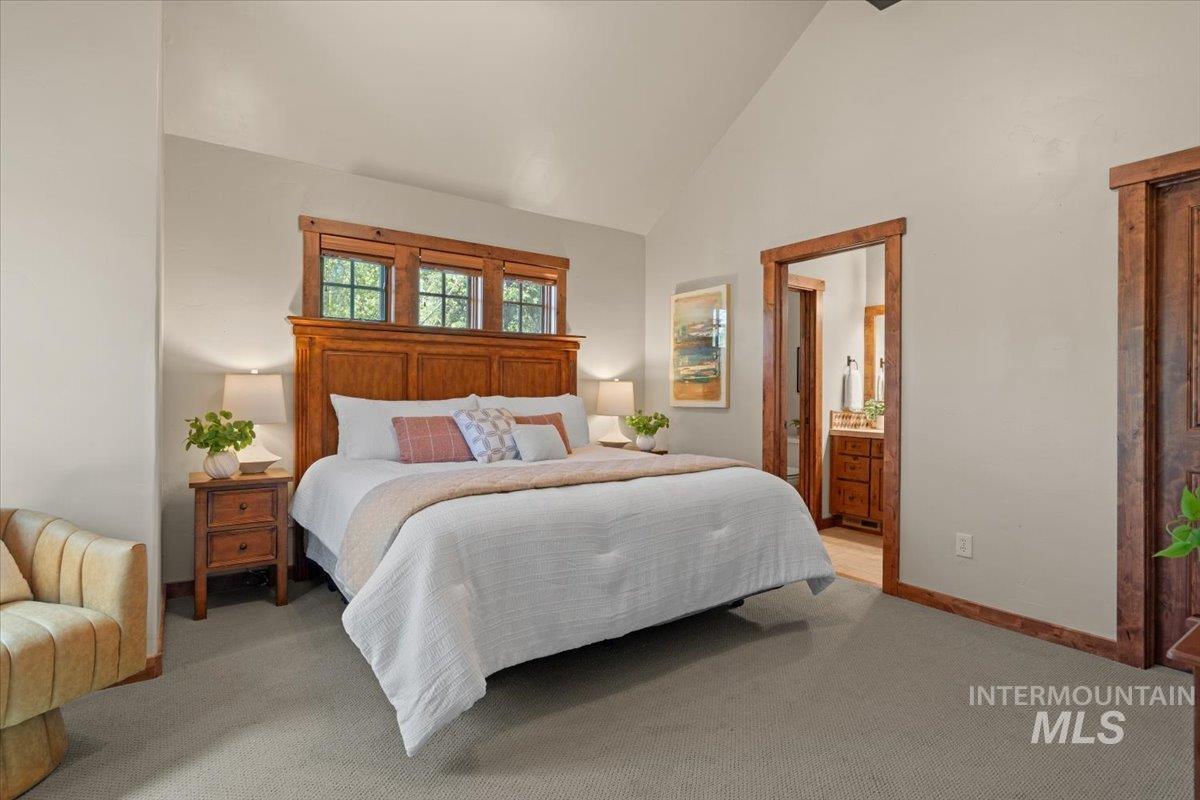 Vaulted ceiling bedroom with wood-trimmed transom windows and an en-suite bathroom featuring a wood vanity