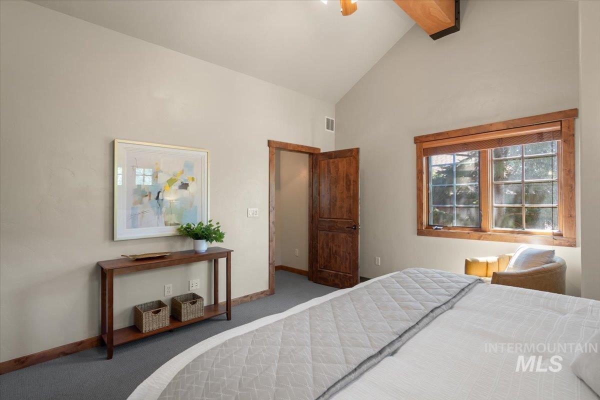 Interior room featuring a vaulted ceiling with exposed wood beams, a window with wood-frame trim, and a wood-finish door