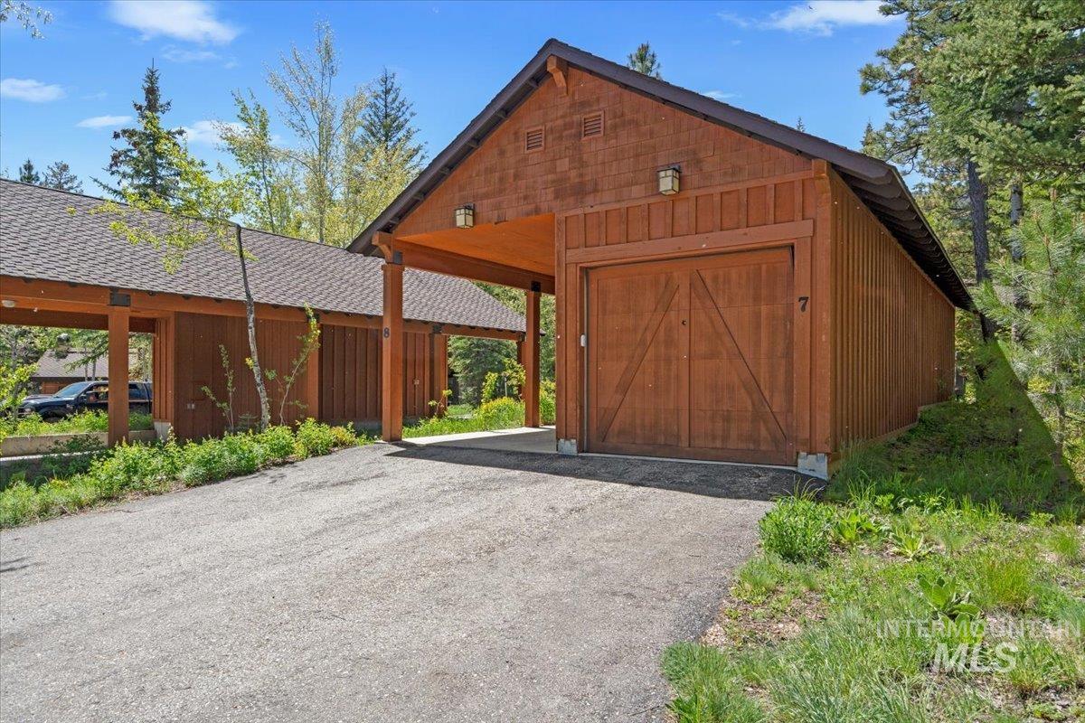 Wood-sided garage building with an attached covered carport and a gravel driveway