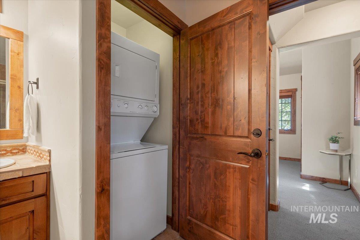 Built-in laundry closet with a stacked washer and dryer, featuring a solid wood panel door with dark hardware
