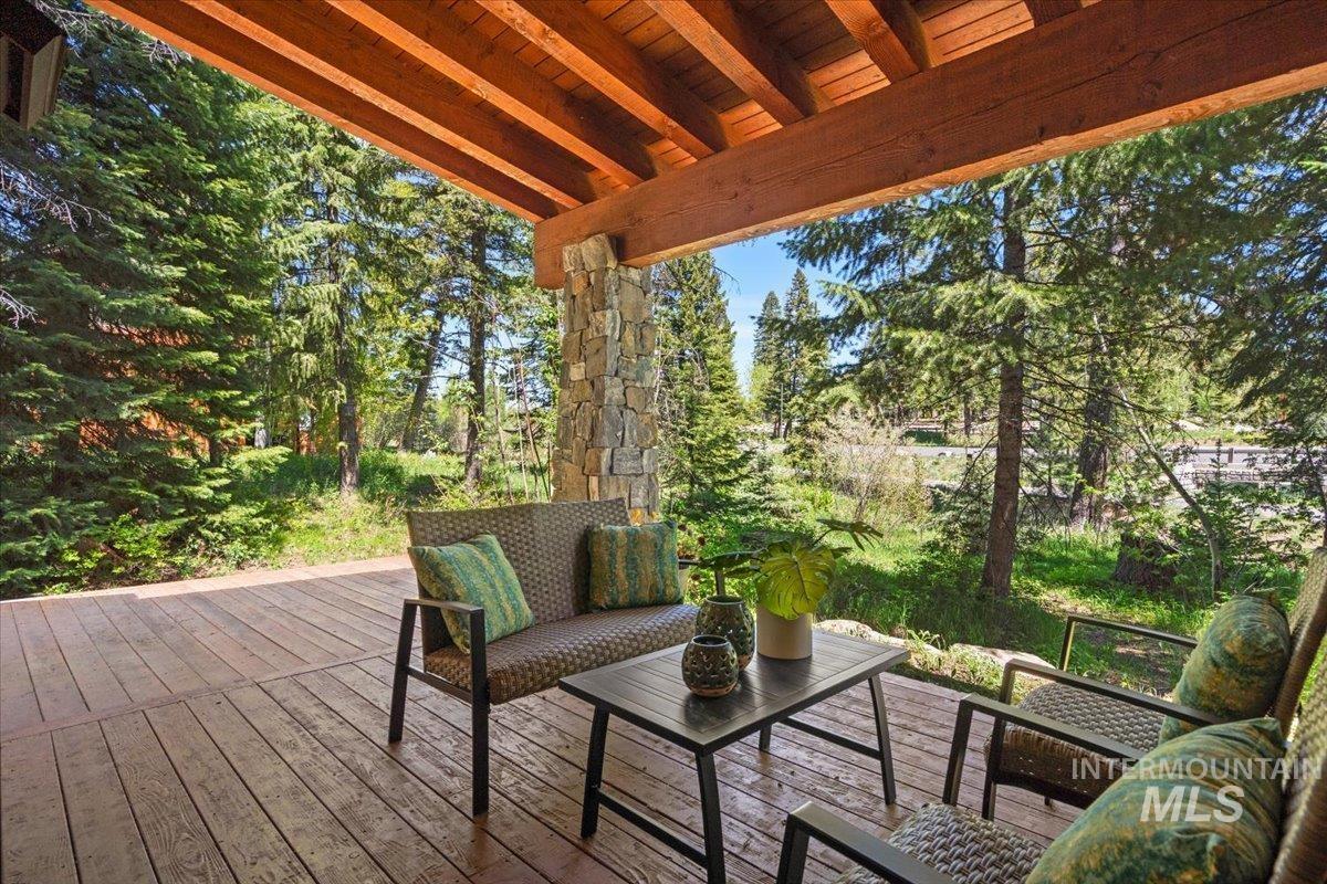 Covered outdoor deck with wood-finish flooring, exposed wood beam ceiling, and a stone pillar