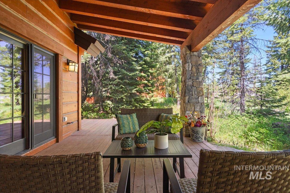 Covered wooden deck featuring exposed wood beam ceiling, stone column, wood siding, and glass sliding doors