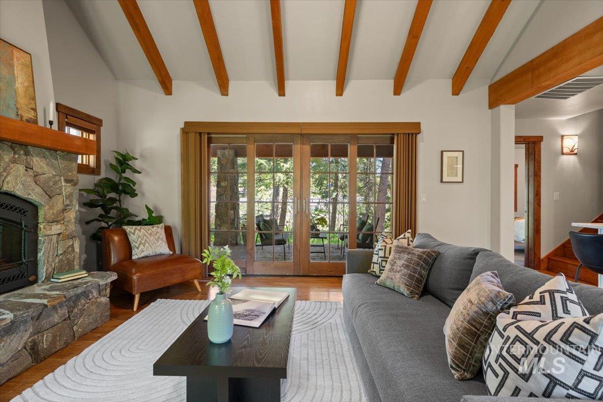 Living area featuring a stone-clad fireplace with wood mantel, vaulted ceiling with exposed wood beams, wood-finish flooring, and sliding glass doors with wood frames opening to exterior space