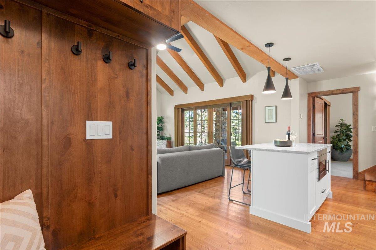Vaulted ceiling with exposed beams, wood-finish flooring, white kitchen island with counter seating, sliding glass doors, and a built-in wood bench with wall hooks