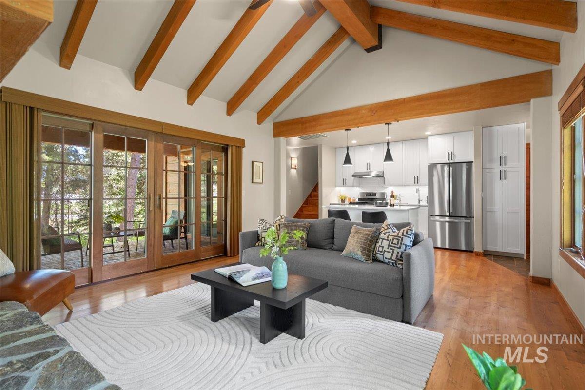 Vaulted ceiling with exposed wood beams, wood-finish flooring, and a stone-clad fireplace base