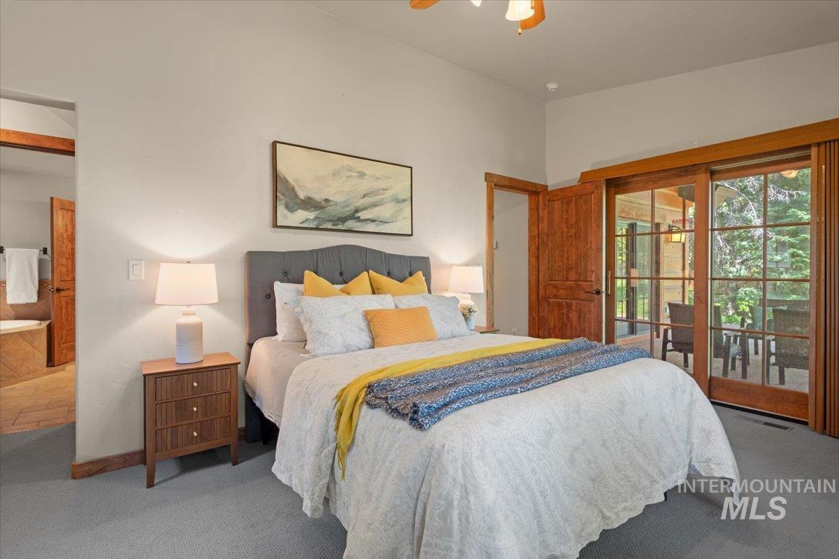 Bedroom featuring vaulted ceilings, wood-finish sliding glass doors opening to a covered patio, a solid wood paneled door, and carpet flooring