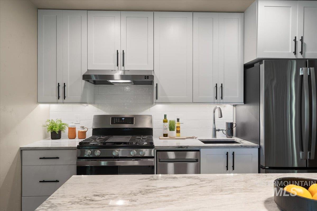 Contemporary kitchen featuring light gray cabinetry with matte black hardware, stainless steel appliances, a subway tile backsplash, and stone-finish countertops