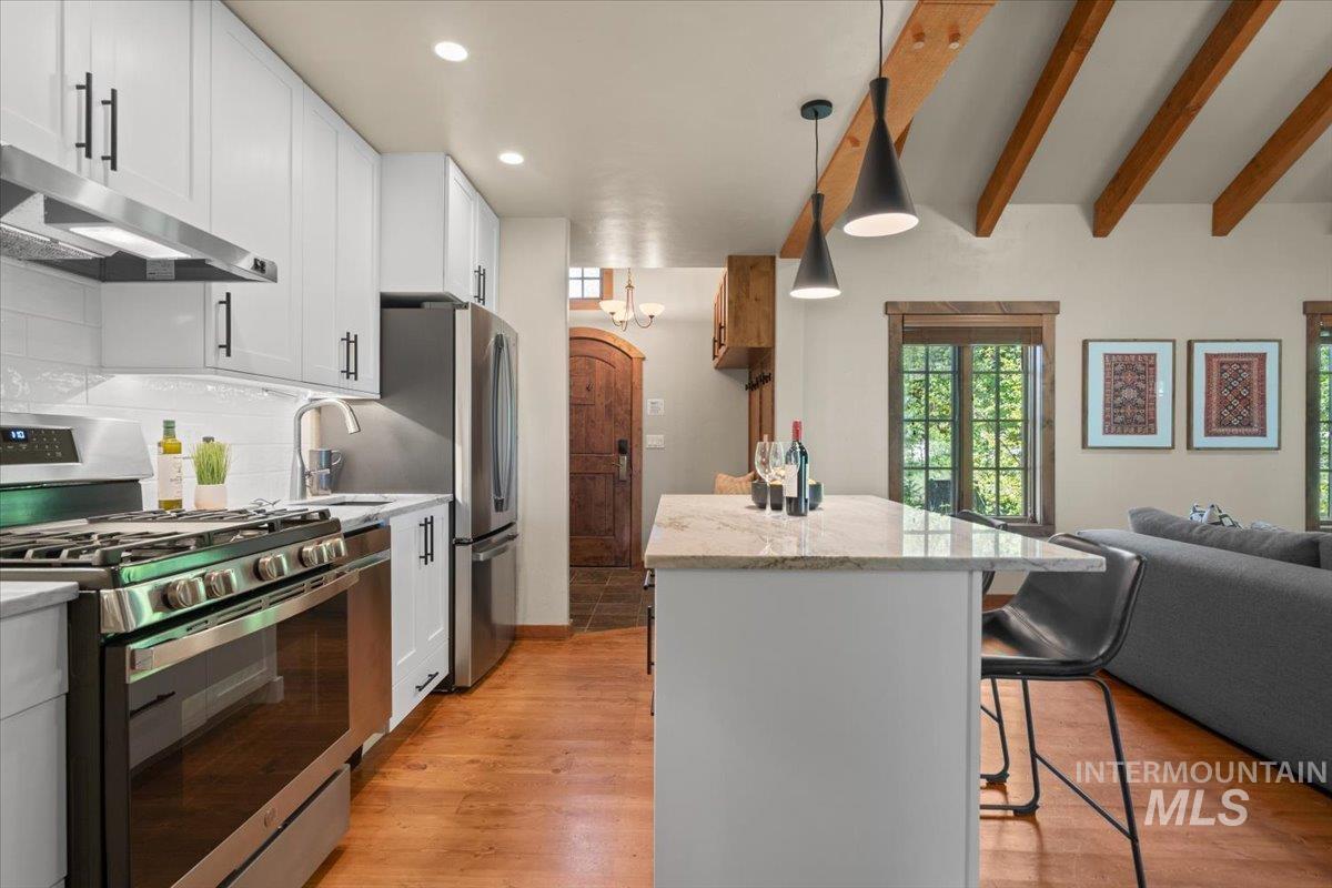 Kitchen featuring white cabinetry, stainless steel appliances, granite island, and wood-finish flooring