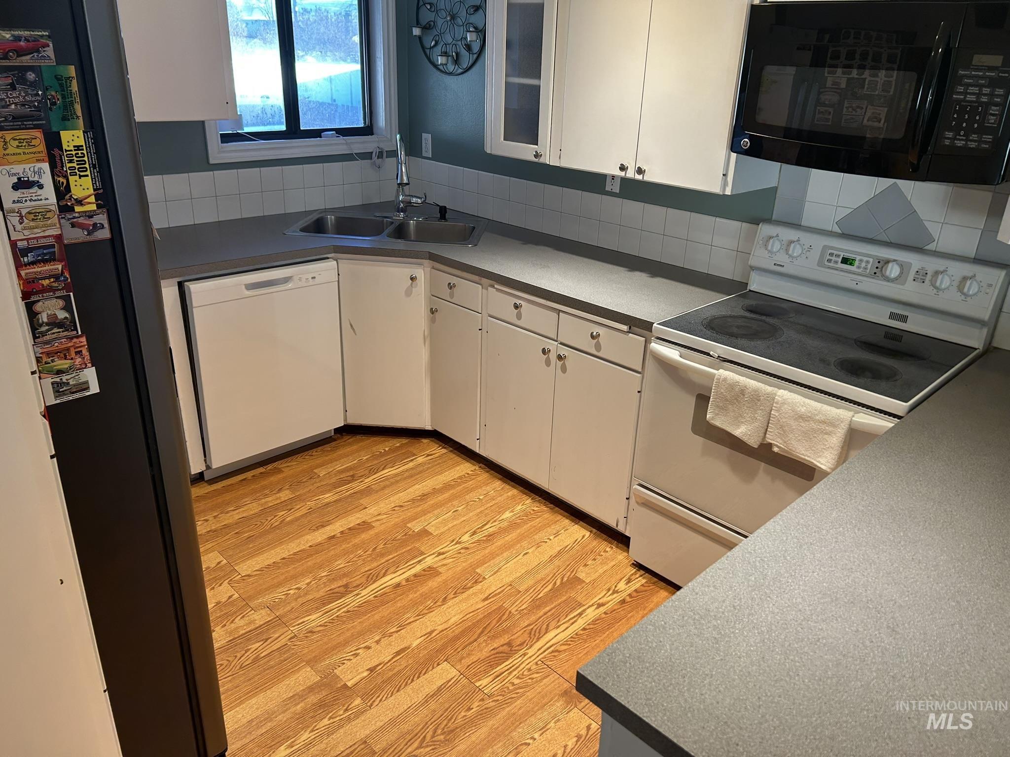 Kitchen with black appliances, white cabinets, light wood finished floors, and decorative backsplash
