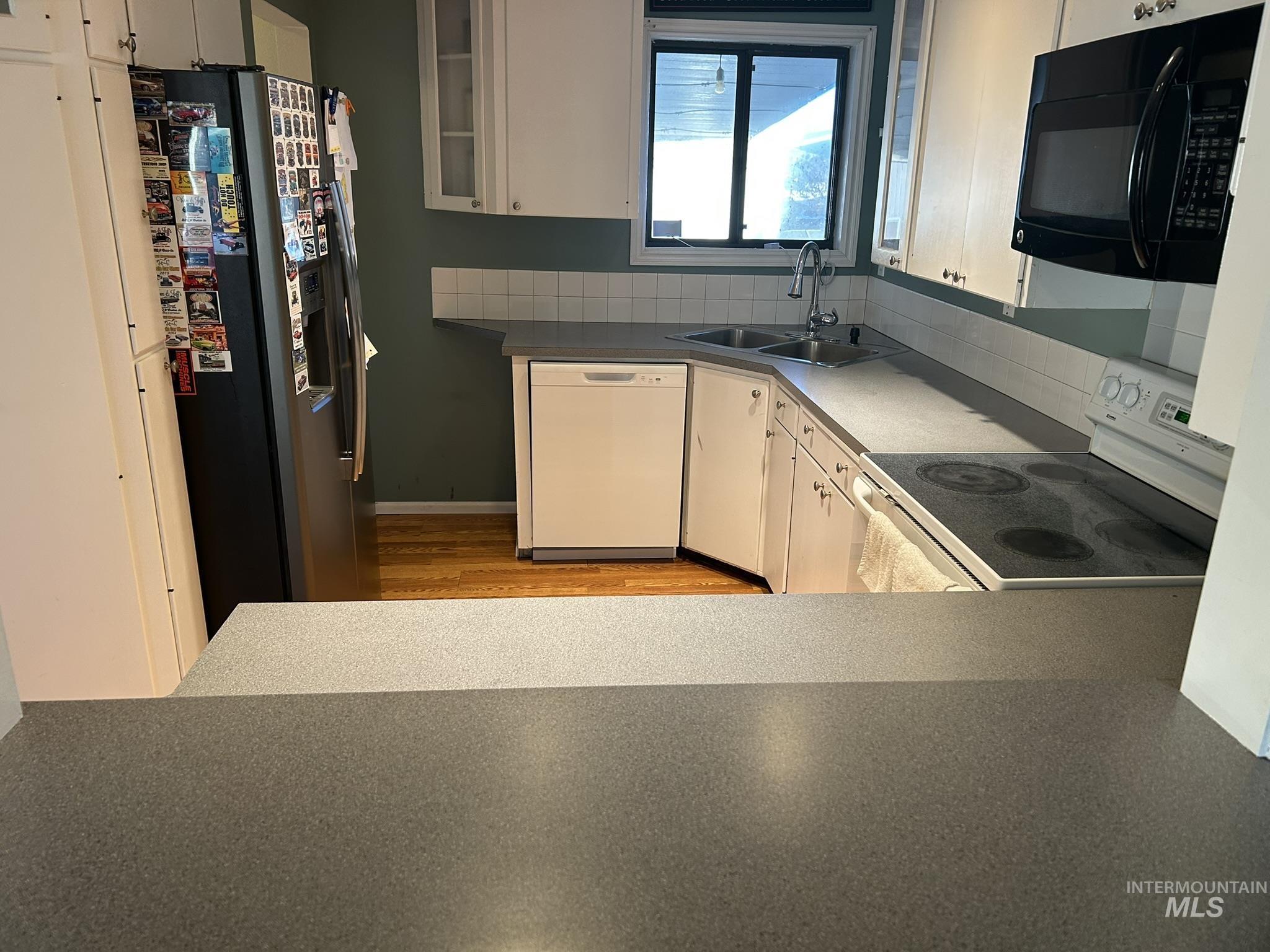 Kitchen featuring white appliances, white cabinets, tasteful backsplash, and light wood-style flooring