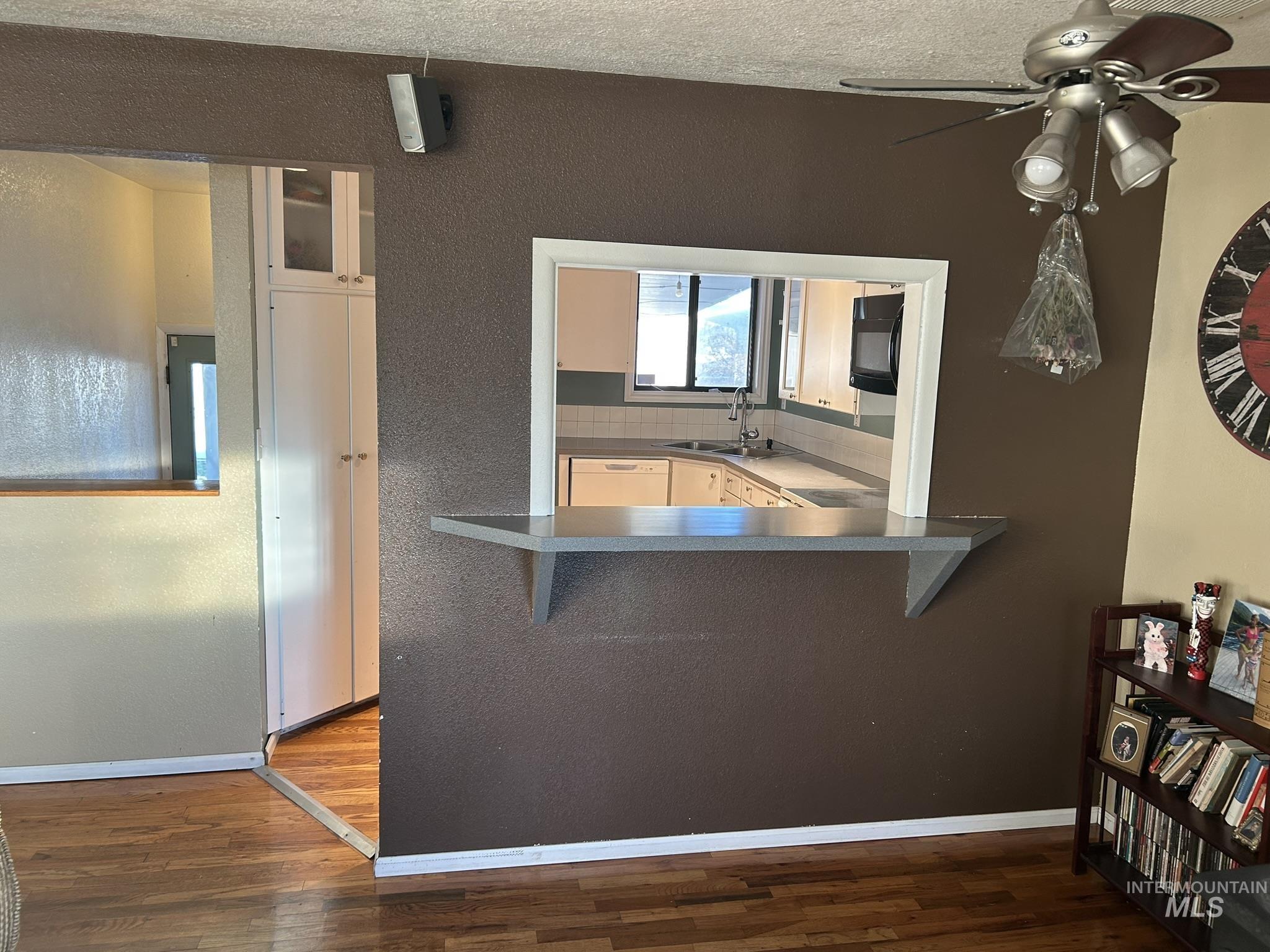Kitchen with a kitchen bar, dark countertops, white dishwasher, dark wood-type flooring, and ceiling fan