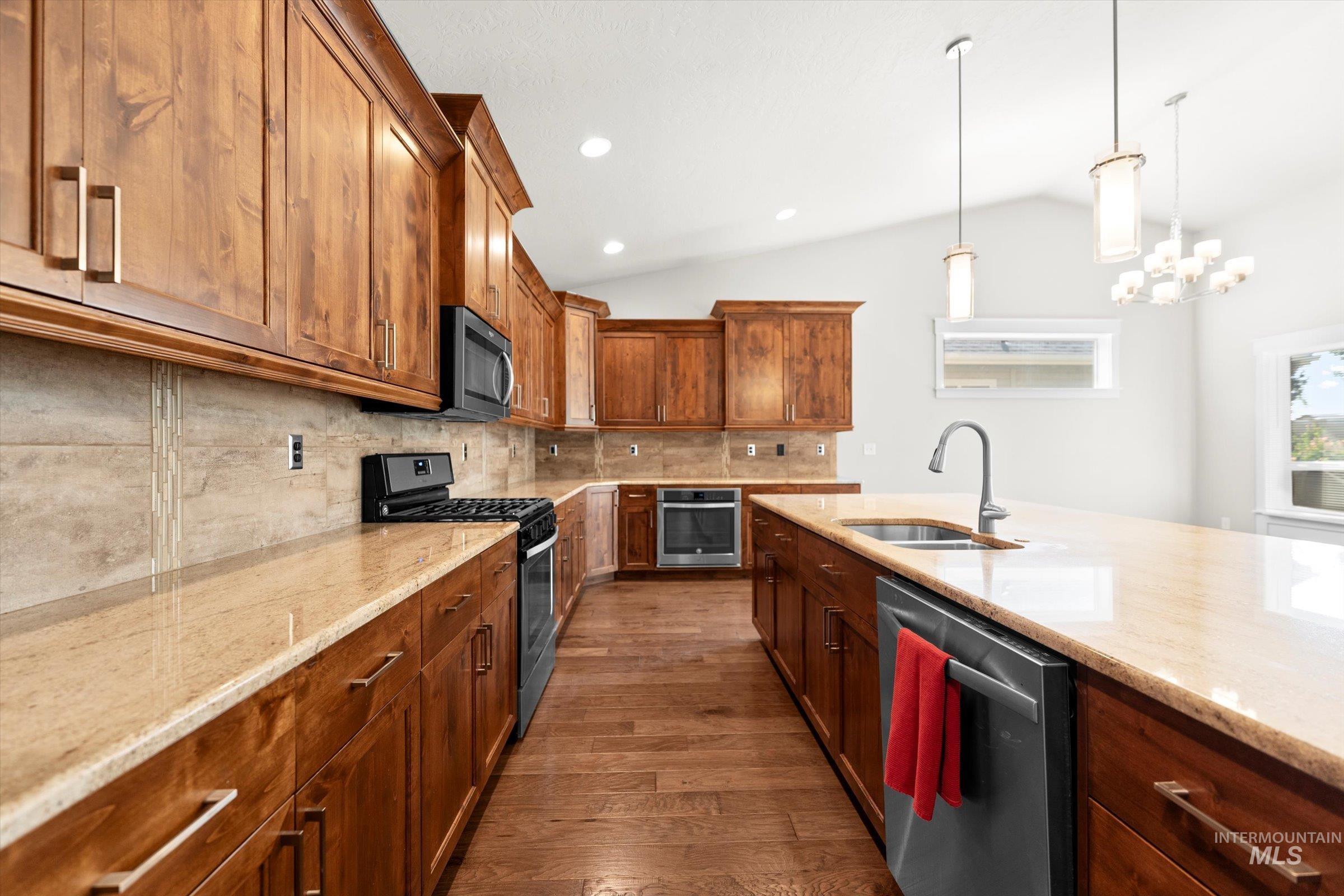 Kitchen featuring tasteful backsplash, appliances with stainless steel finishes, dark wood-type flooring, light stone counters, and lofted ceiling