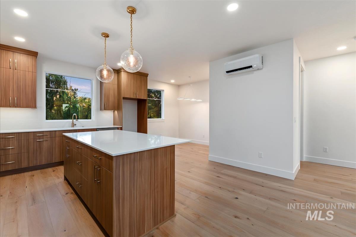 Kitchen featuring an expansive island with a white countertop, wood-finish cabinetry, light wood-finish flooring, recessed lighting, and a ductless mini-split system