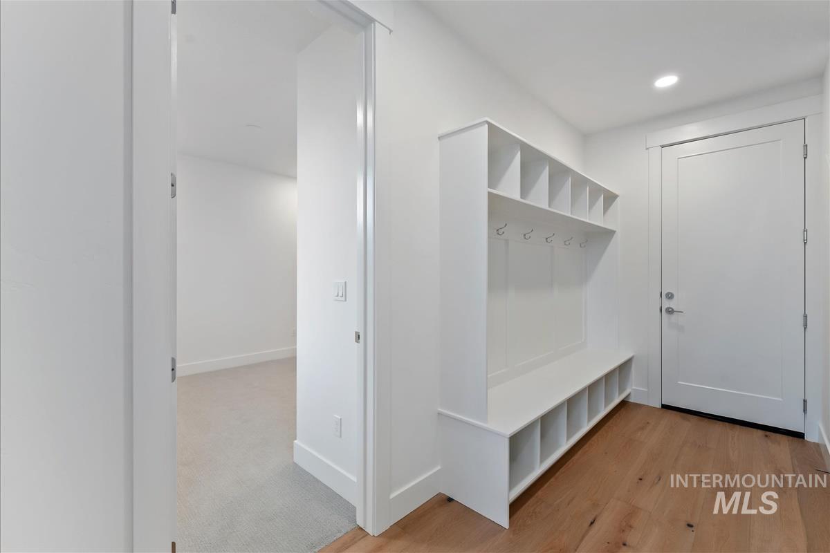 Entryway featuring built-in white cabinetry with cubbies and coat hooks, wood-finish flooring, recessed lighting, and a solid white door with brushed nickel hardware