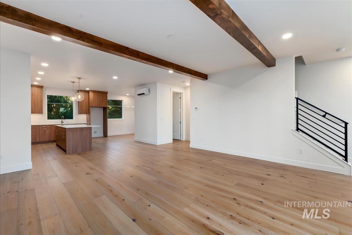 Spacious open-concept interior featuring light wood-finish flooring, exposed ceiling beams, and recessed lighting
