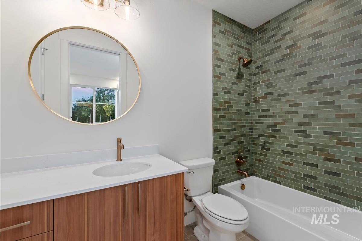 Bathroom featuring a wood-finish vanity with a white countertop and undermount sink, a circular mirror with a gold-tone frame, green subway tile shower surround, and bronze-tone fixtures
