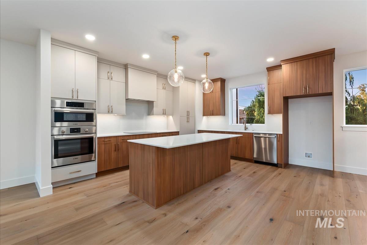 Gourmet kitchen featuring a central island with a white countertop, wood-finish flooring, stainless steel double ovens, and mixed-tone cabinetry