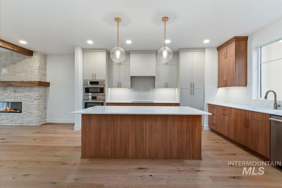 Kitchen featuring a large central island with a white countertop and wood-finish paneling, complemented by dual pendant lights