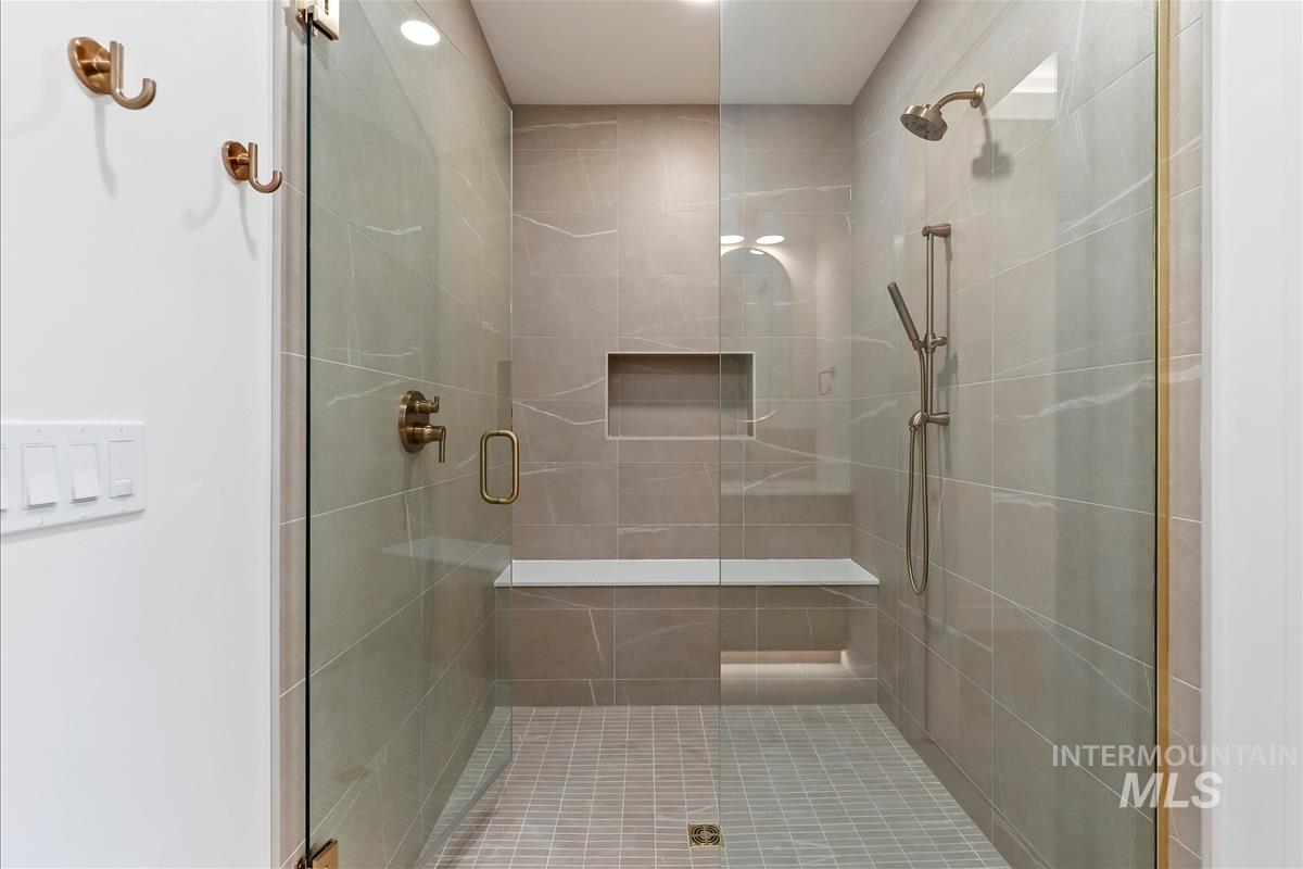 Glass-enclosed shower with full tile surround, integrated bench, and recessed shelving