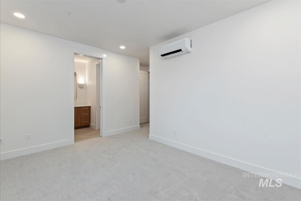 Spacious room featuring light-toned carpeting, recessed lighting, and a wall-mounted mini-split HVAC unit