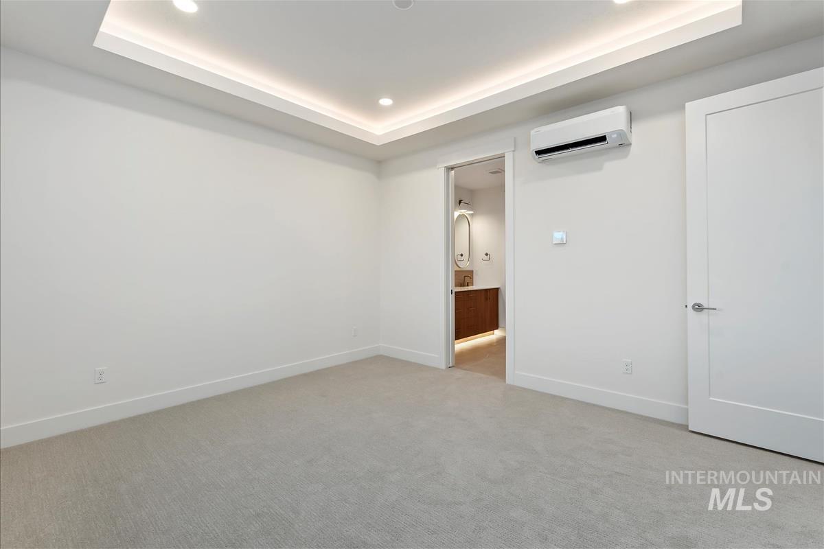 Recessed lighting and cove lighting illuminate a neutral-toned room with light gray carpeting