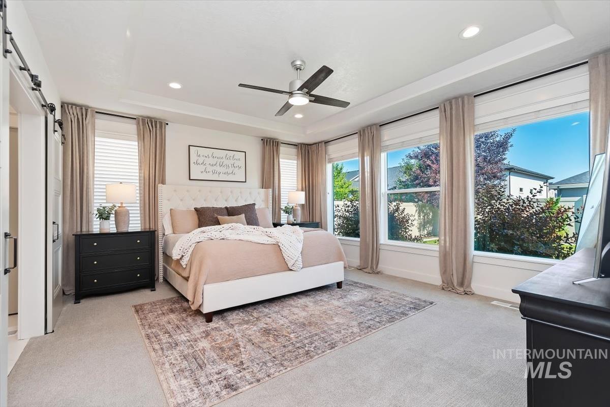 Spacious bedroom featuring light-toned carpeting and a tray ceiling with recessed lighting