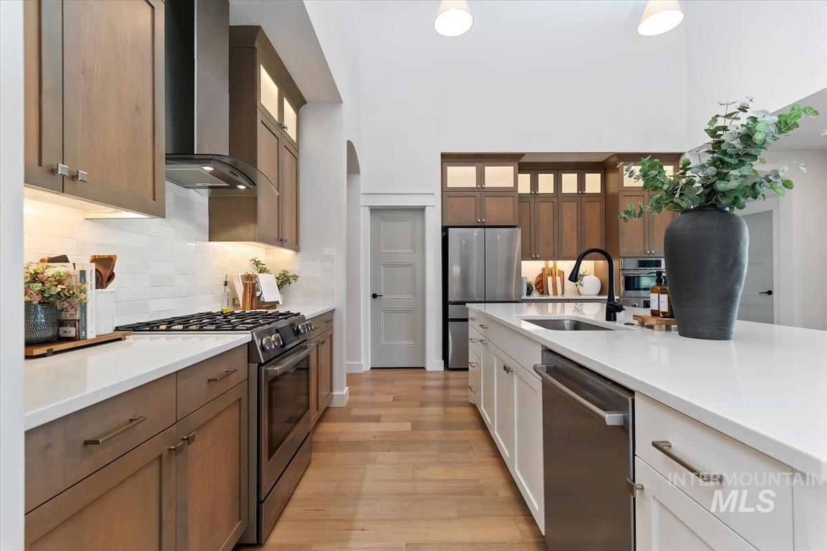 Gourmet kitchen featuring a spacious island with an undermount sink and matte black faucet, stainless steel appliances, a gas range with a modern vent hood, two-tone cabinetry, and wood-finish flooring