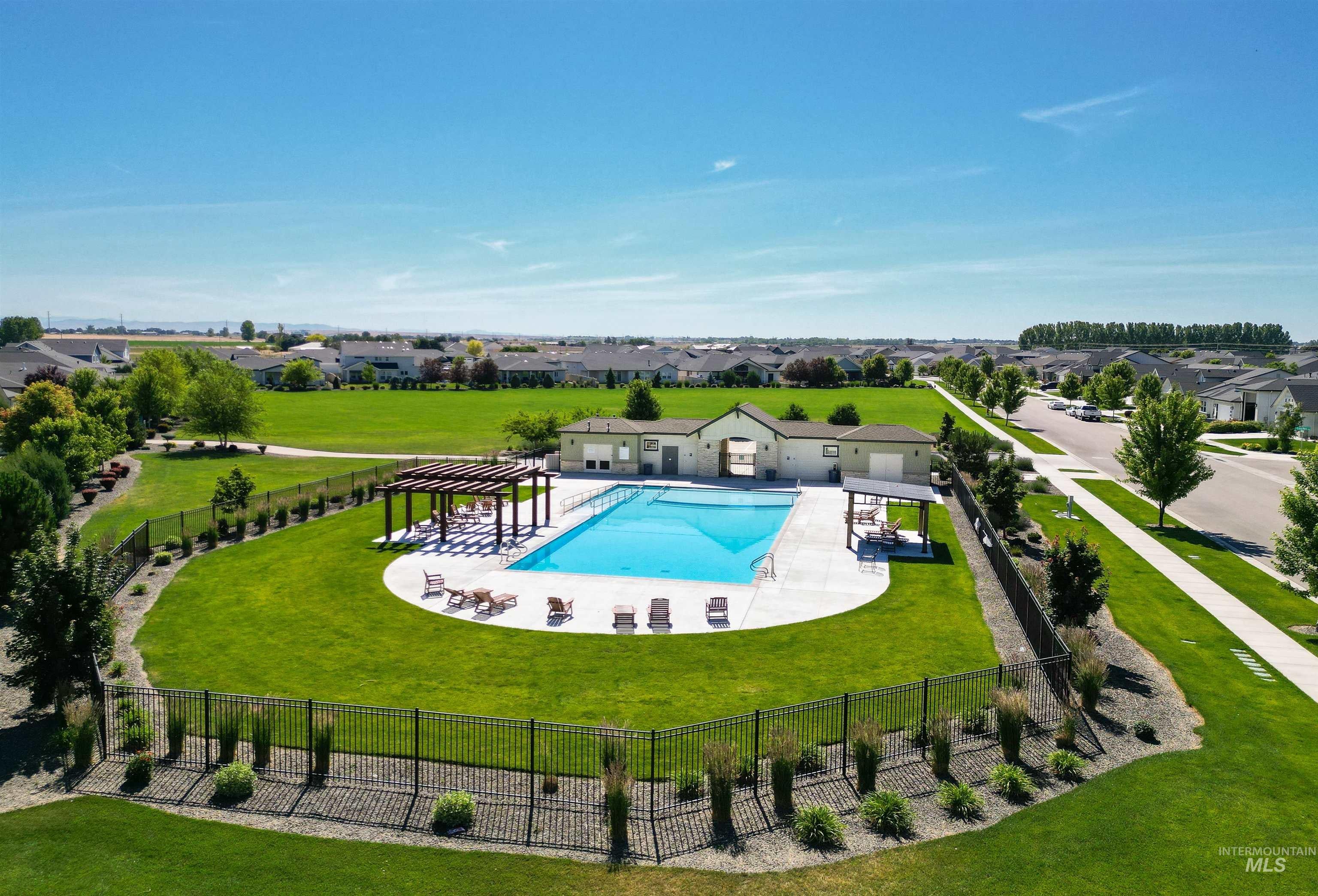 Community pool featuring a large concrete deck, perimeter fencing, and an adjacent pergola-covered lounge area