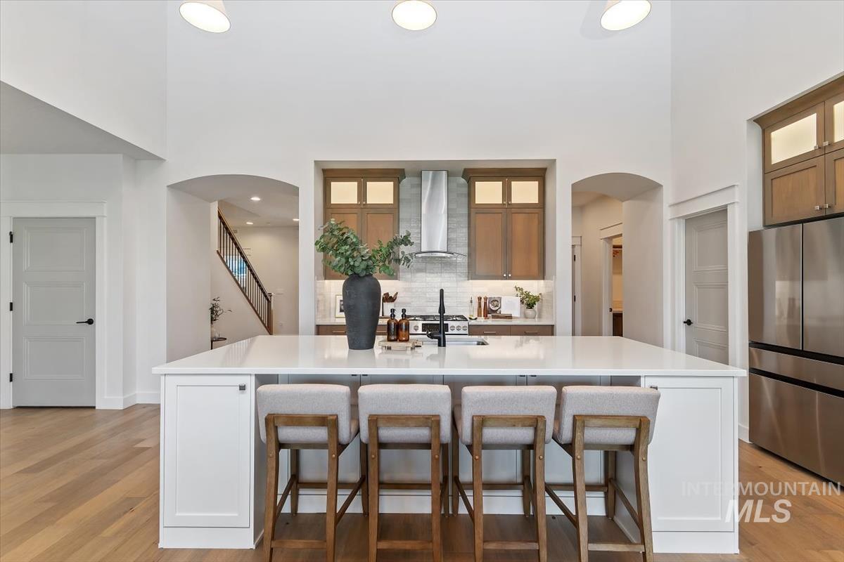 Kitchen island with white countertop and integrated seating, featuring a stainless steel range hood, light wood-finish flooring, and vaulted ceilings