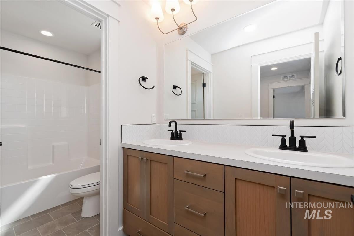 Bathroom featuring a double vanity with wood-finish cabinetry, white countertops, and black fixtures