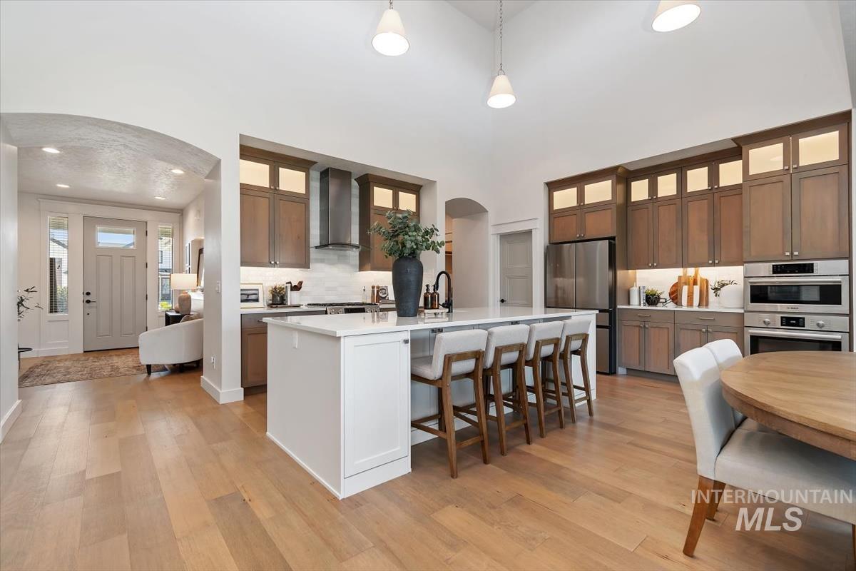 Kitchen featuring a large island with seating, stainless steel appliances, wood-finish flooring, vaulted ceiling, and recessed lighting