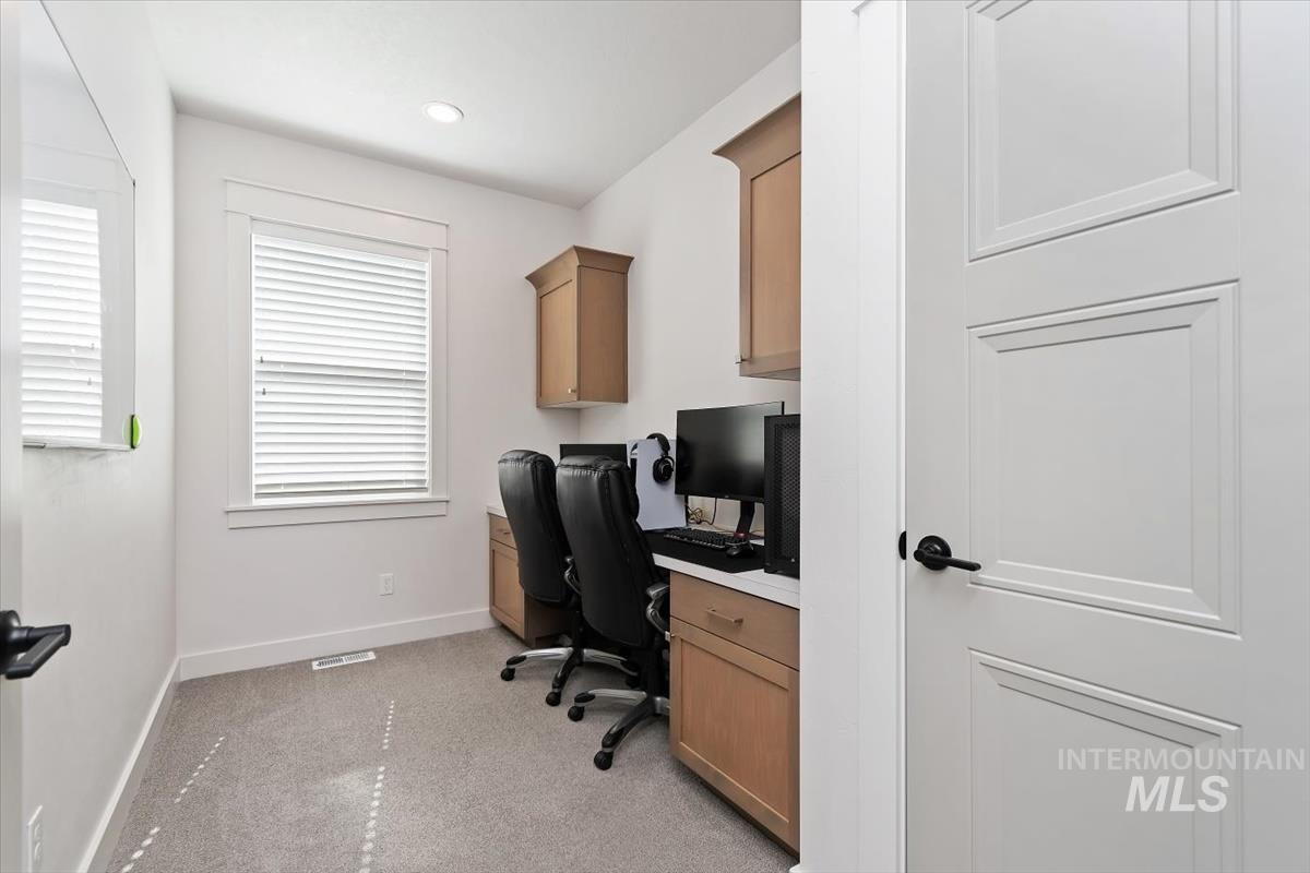 Dedicated workspace featuring light-toned cabinetry, a built-in desk, and soft carpeting
