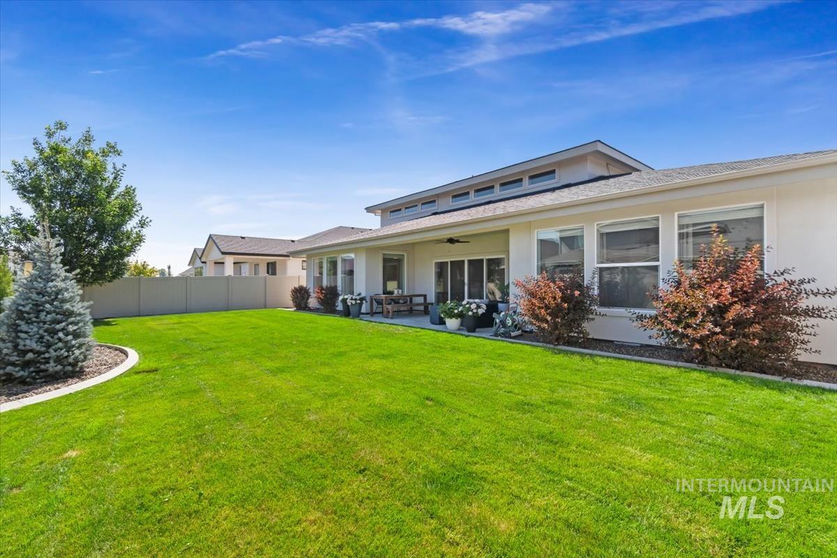 Expansive backyard featuring a manicured lawn, established landscaping, and a covered patio