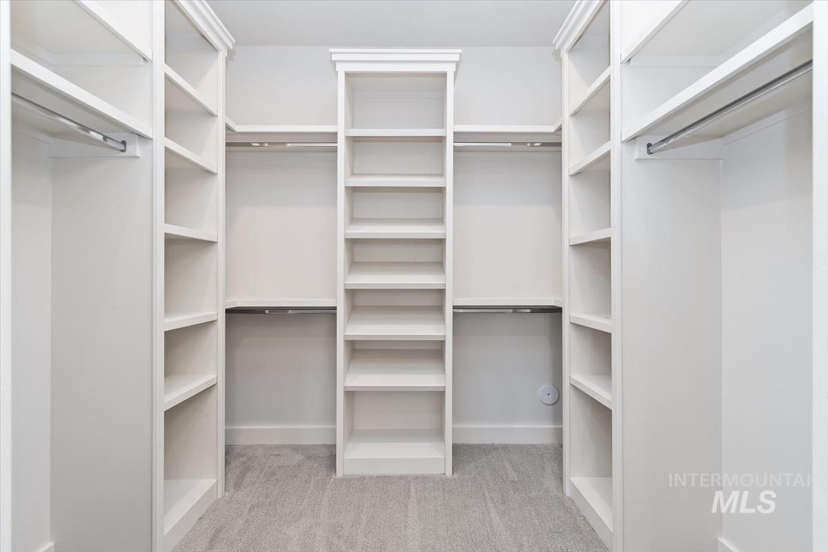Custom closet system featuring extensive shelving, multiple hanging rods, crown molding, and grey carpet flooring