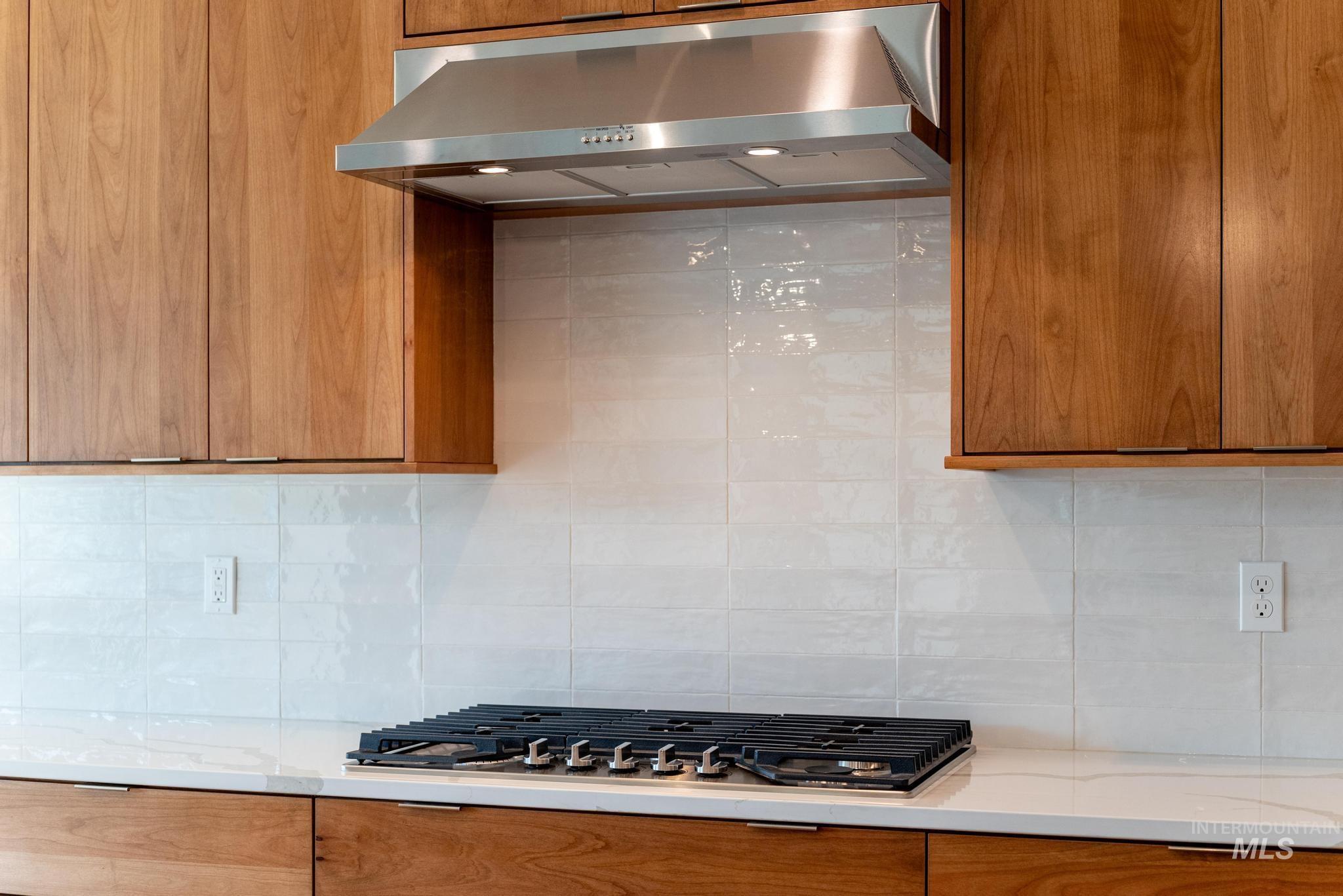 Kitchen with under cabinet range hood, tasteful backsplash, and brown cabinetry