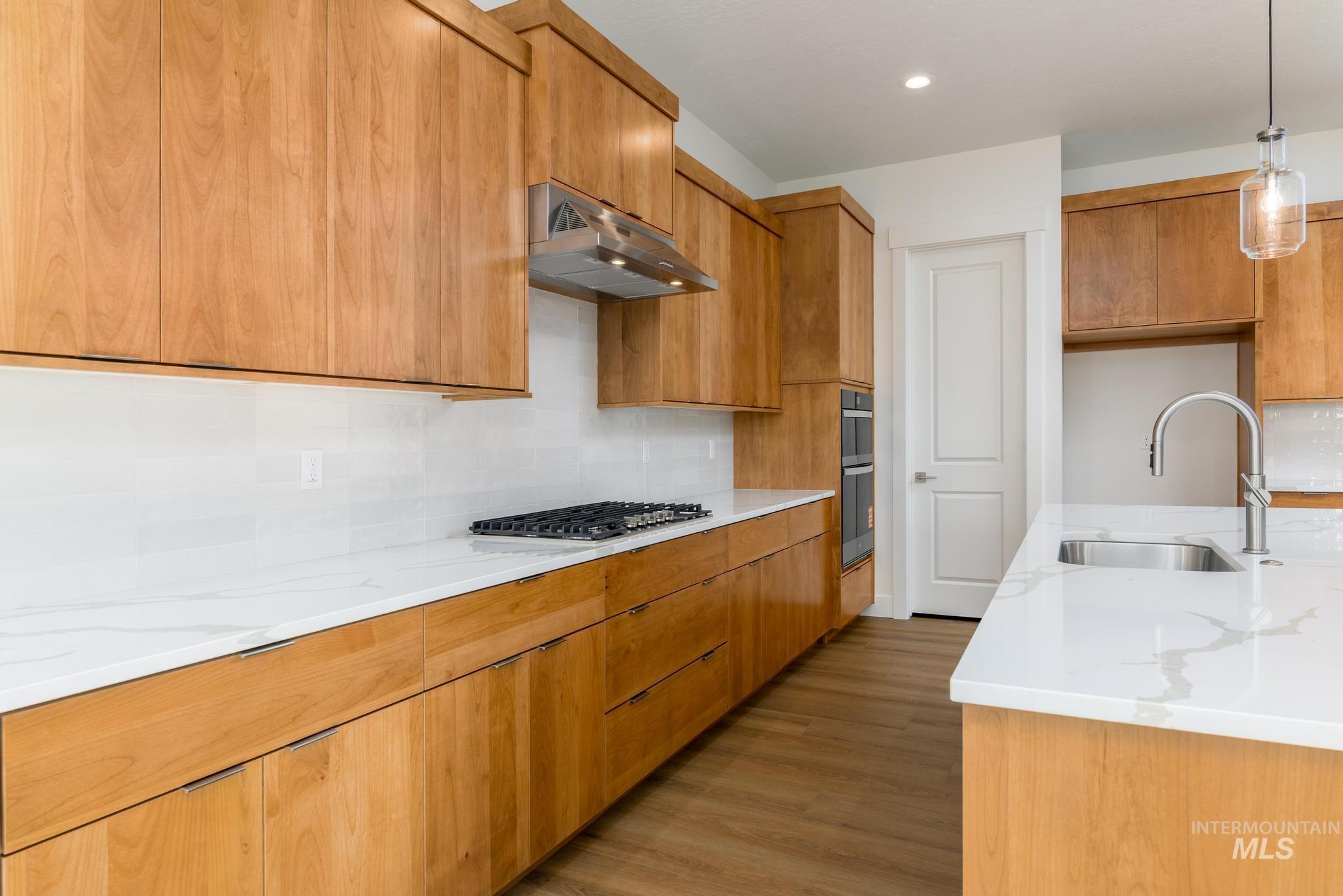 Kitchen featuring decorative light fixtures, light stone counters, brown cabinetry, light wood-style flooring, and tasteful backsplash