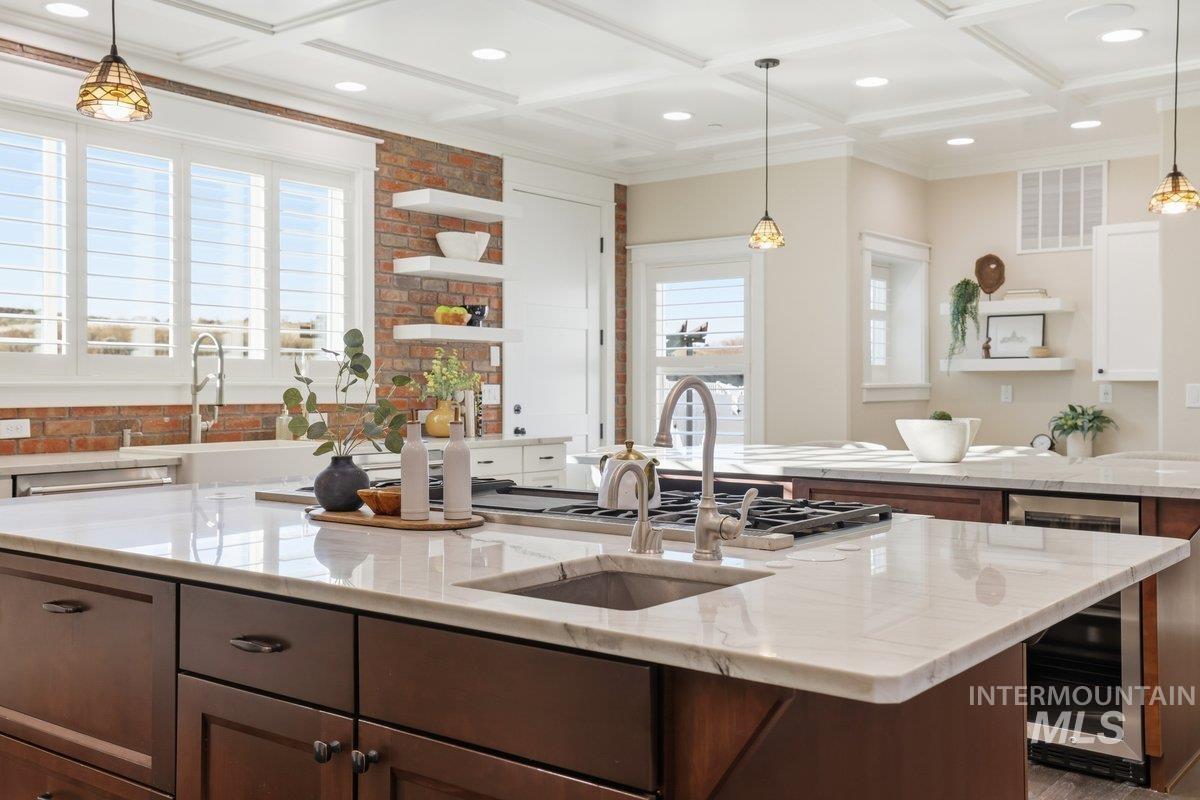 Kitchen with open shelves, pendant lighting, wine cooler, light stone countertops, and beam ceiling