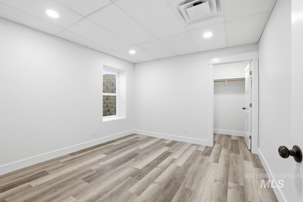 Unfurnished bedroom featuring a spacious closet, a paneled ceiling, light wood-style flooring, and recessed lighting