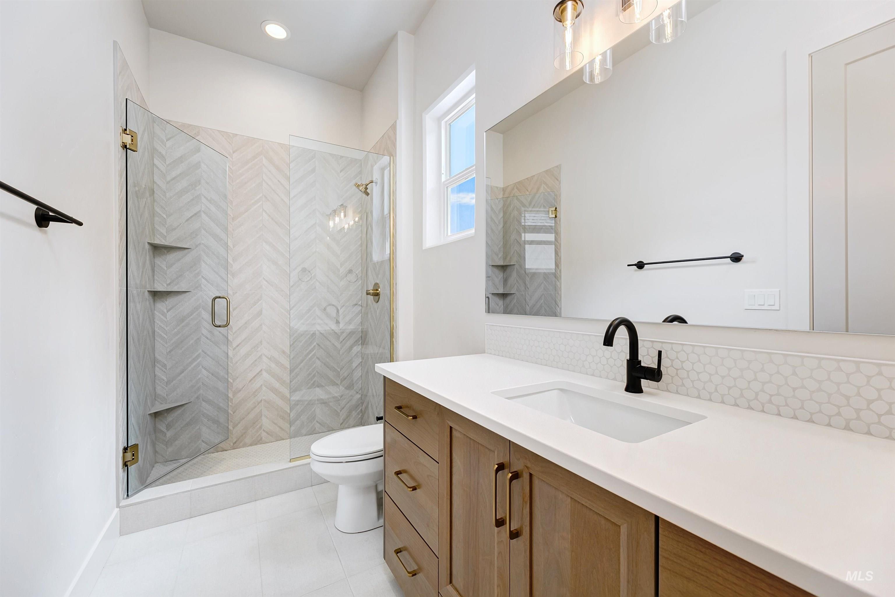 Bathroom featuring a spacious walk-in shower with herringbone tile, a floating wood-finish vanity with a single basin, a large rectangular mirror, and a black wall-mounted faucet