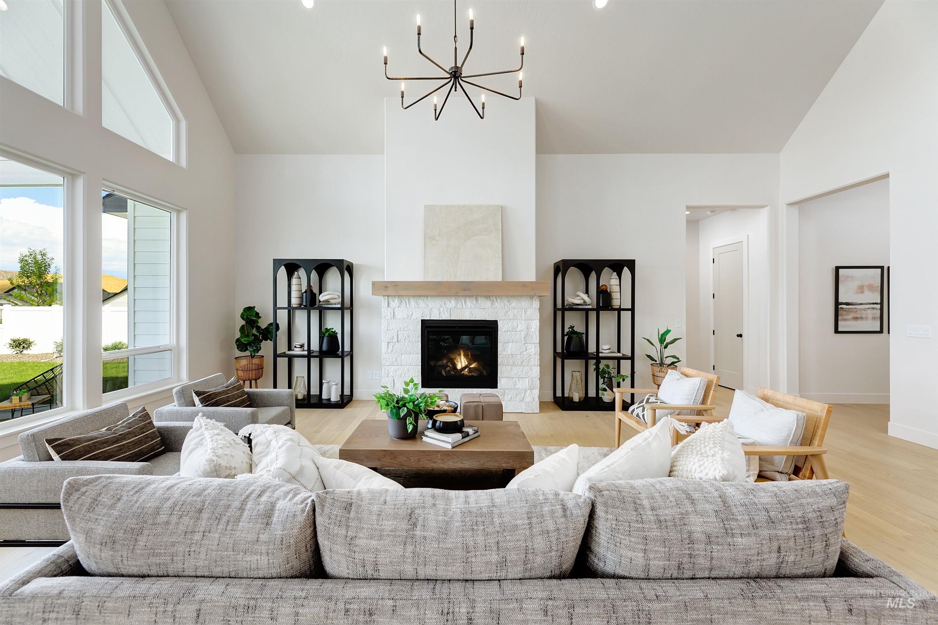 Vaulted living room with a linear fireplace, stone surround, wood mantel, and a multi-arm chandelier