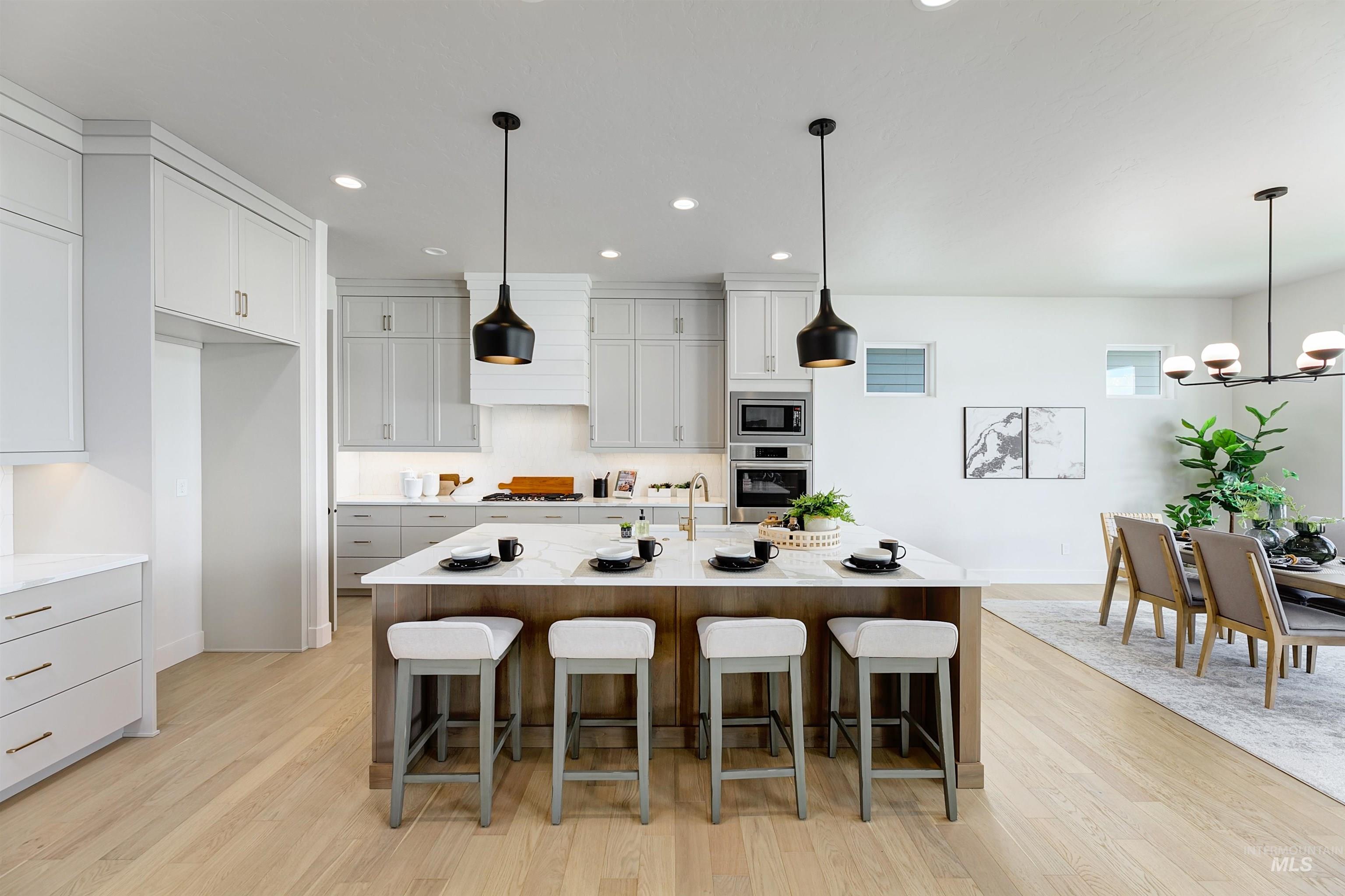 Gourmet kitchen featuring a large central island with seating, built-in stainless steel appliances, light wood-finish flooring, white upper and gray lower cabinetry, and recessed lighting
