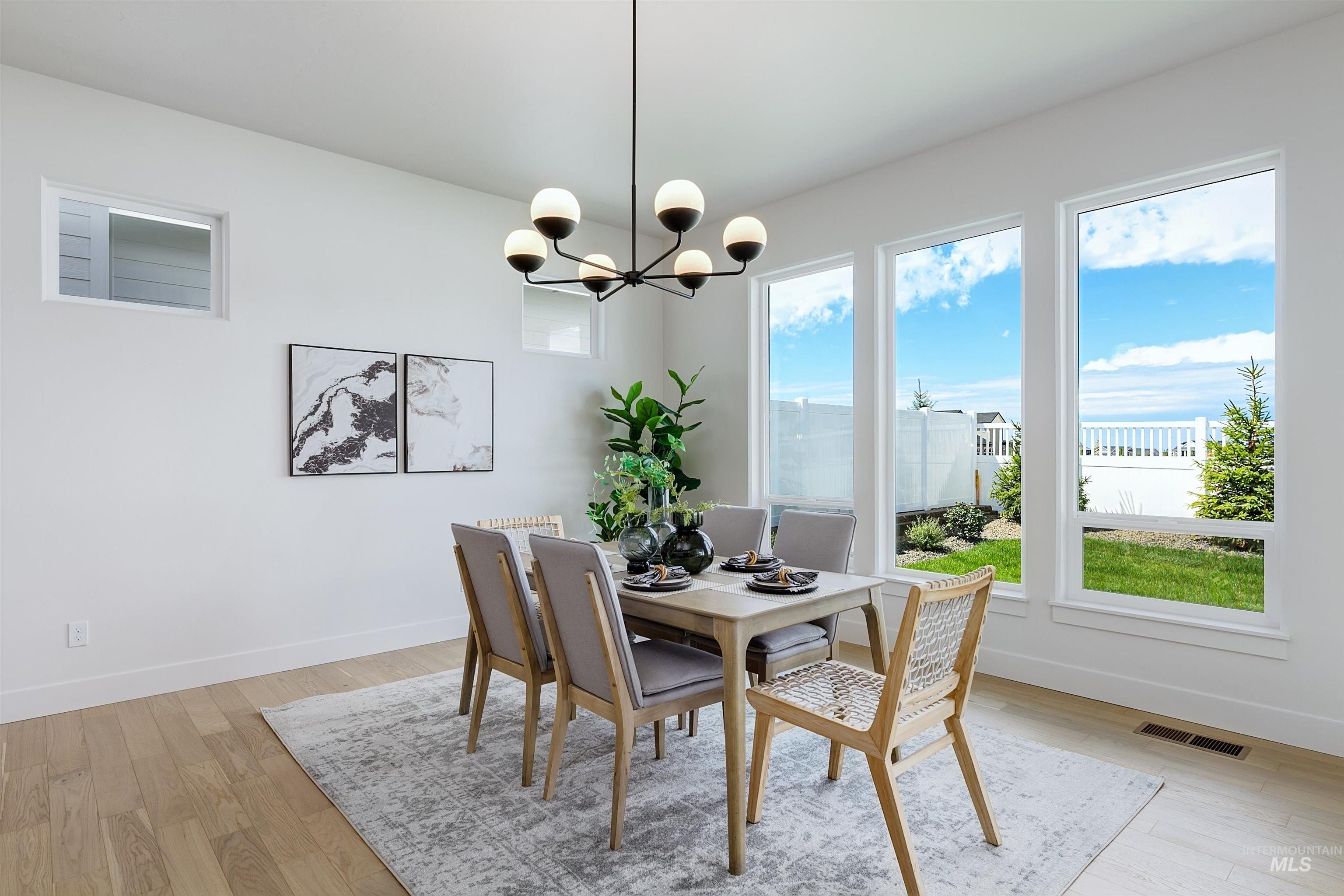 Dining area featuring a contemporary chandelier with globe lighting, light wood-finish flooring, and multiple tall windows providing abundant natural light