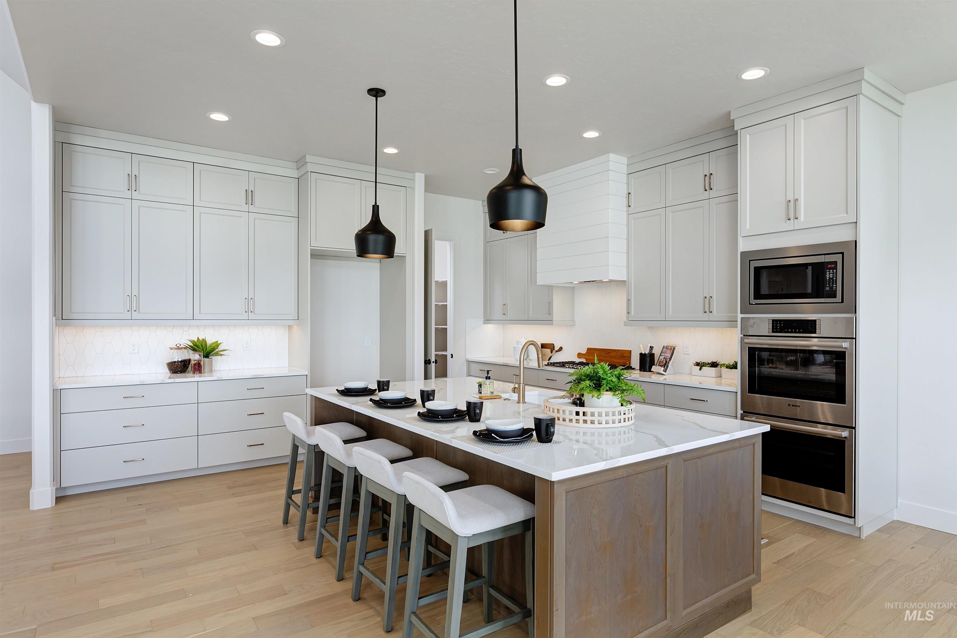 Kitchen featuring a large central island with seating, white shaker-style cabinetry, light wood-finish flooring, stainless steel appliances, and pendant lighting fixtures