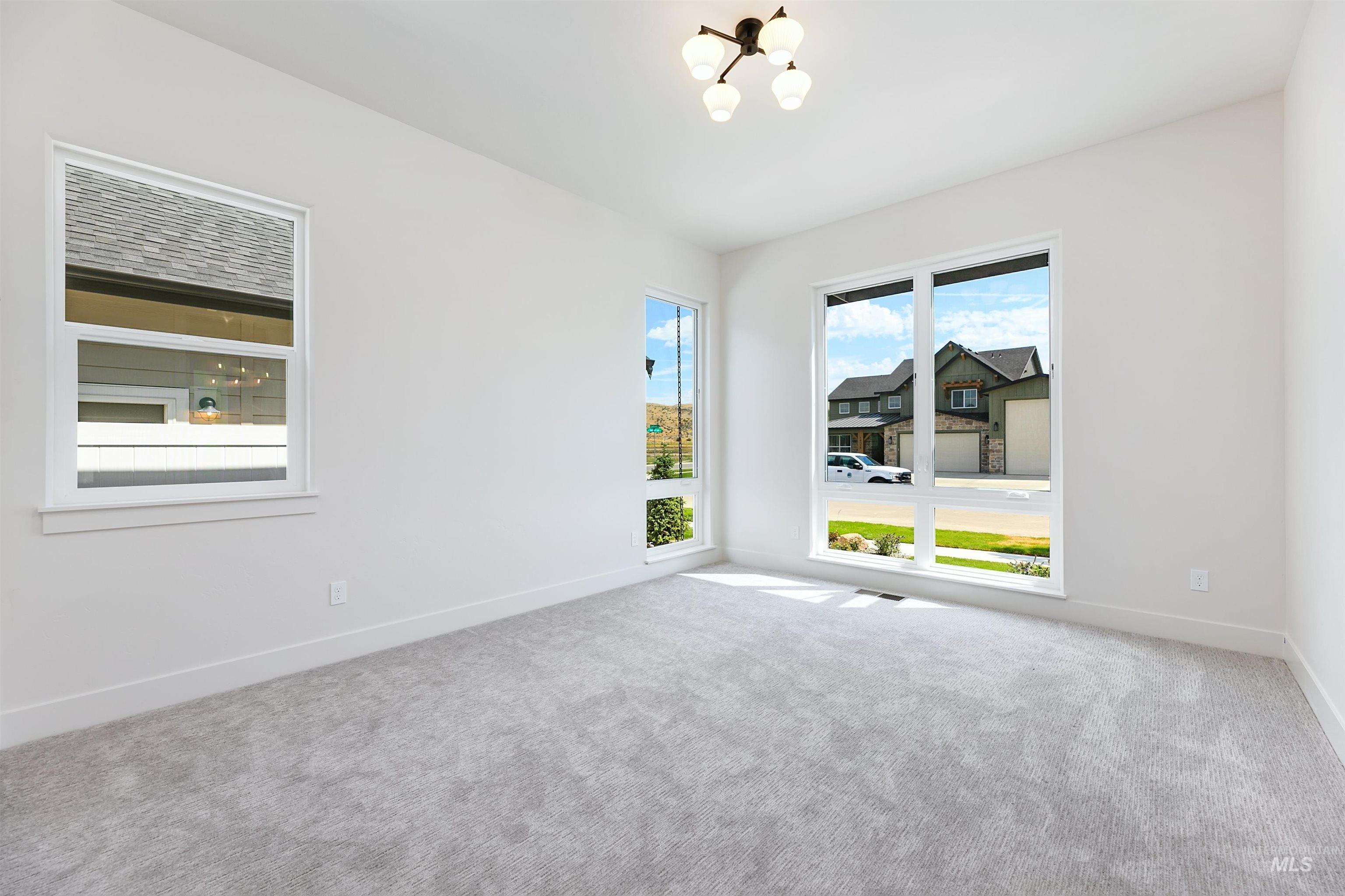 Bright room featuring light gray carpeting, crisp white walls, multiple windows, a modern ceiling light fixture, and wide baseboards
