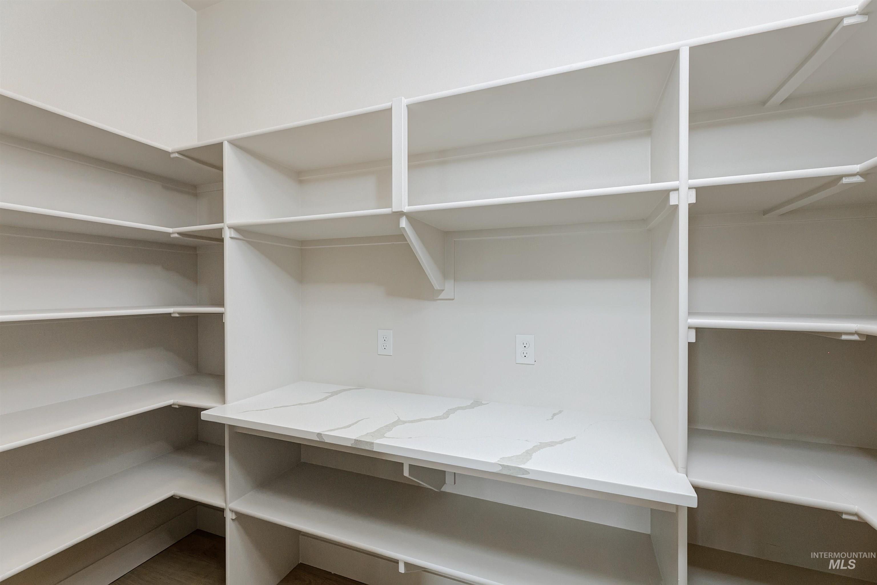 Walk-in pantry featuring extensive white shelving, a white countertop with gray veining, and integrated electrical outlets