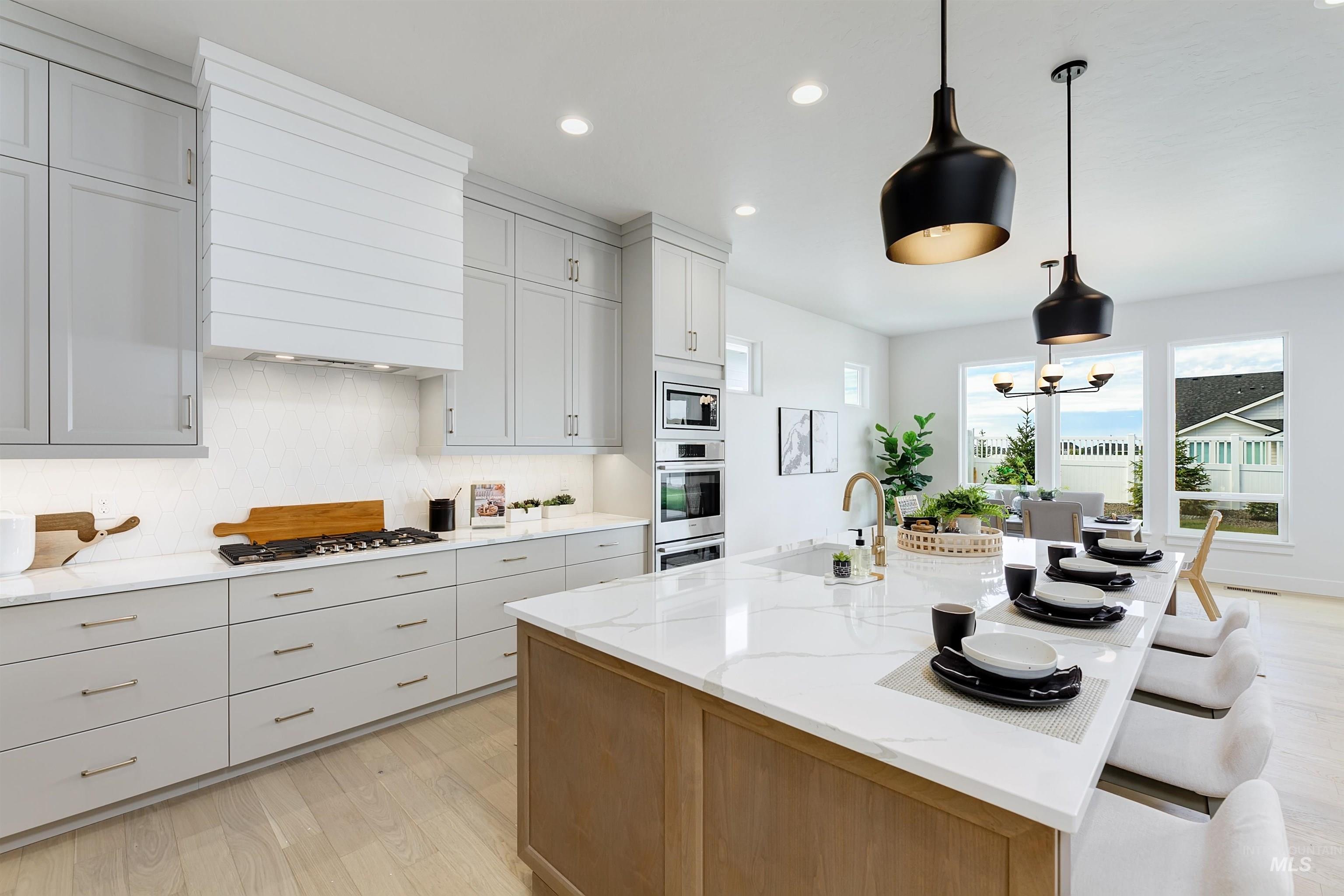 Open-concept kitchen featuring an expansive island with seating, a gas cooktop, light-toned wood-finish flooring, light gray cabinetry, and a white shiplap range hood