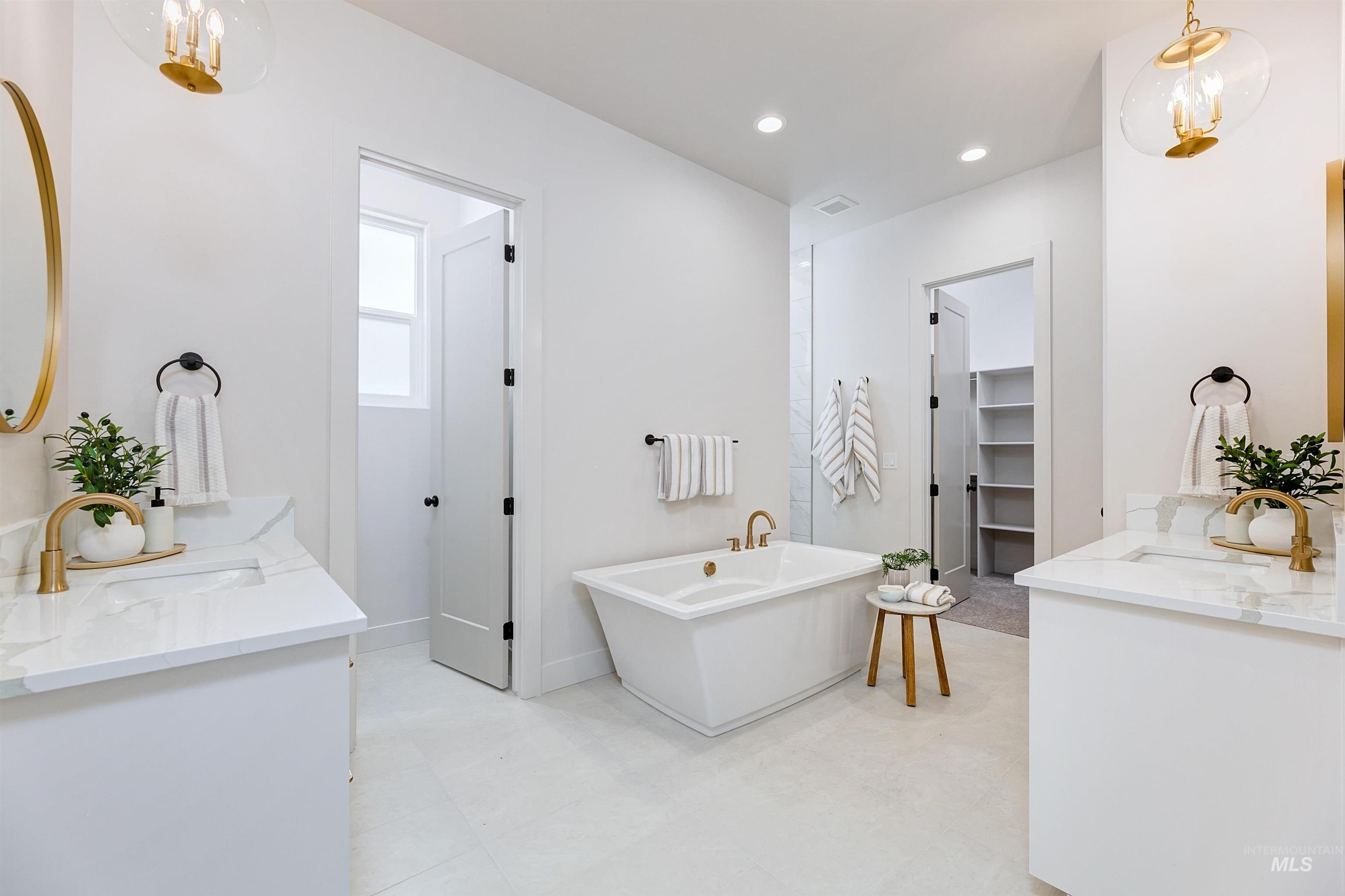 Freestanding soaking tub with brushed gold fixtures, dual vanity sinks with white stone countertops, recessed lighting, and a separate water closet