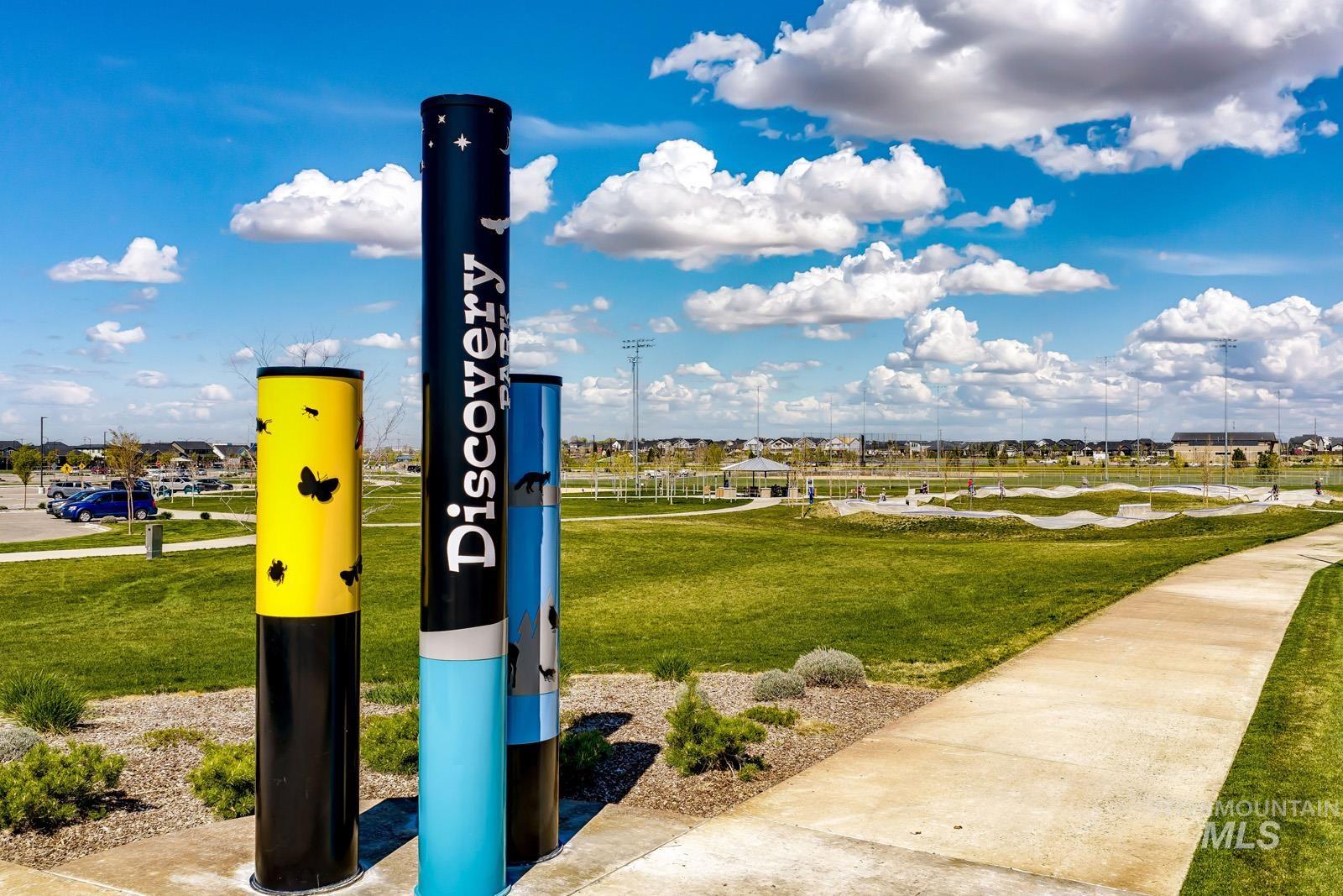 "Discovery Park" signage with a wide concrete pathway, expansive green lawn, and distant recreational facilities
