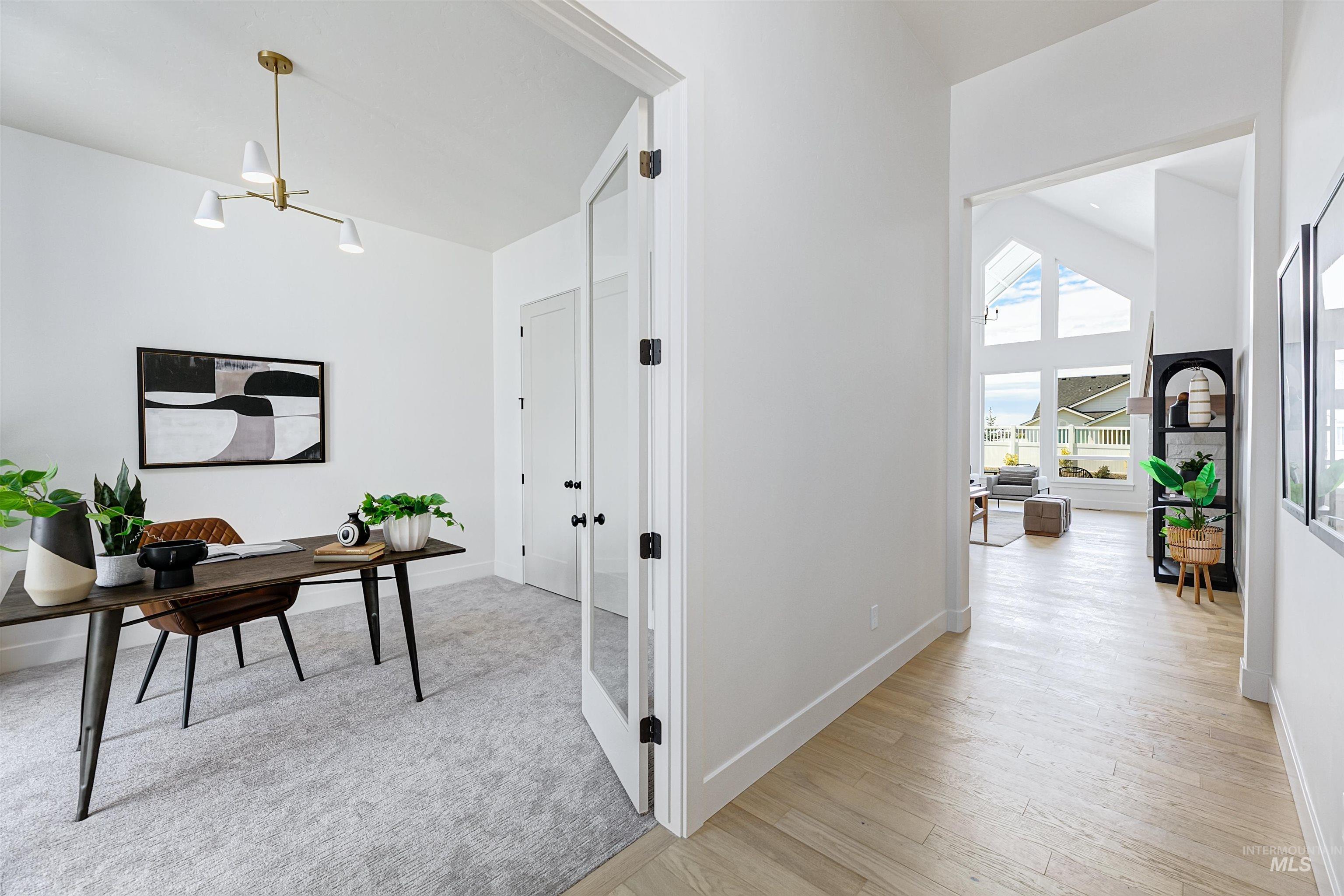 Bright interior featuring an entryway with wood-finish flooring, a dedicated room with a contemporary chandelier, glass-paneled double doors, and a distant great room with vaulted ceilings and expansive windows
